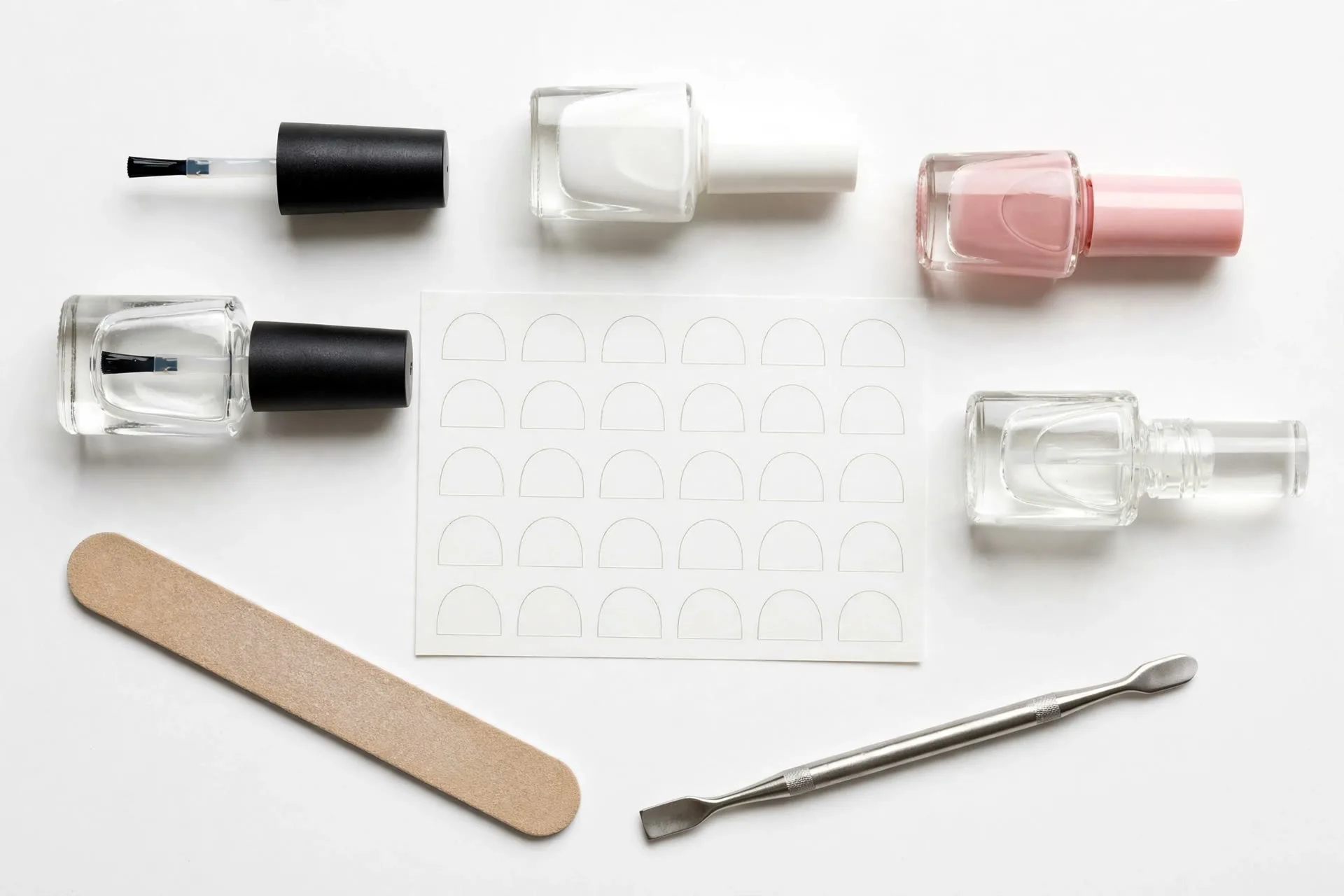 Flatlay of French manicure essentials: base coat, white polish, sheer pink polish, guide stickers, nail file and cuticle pusher