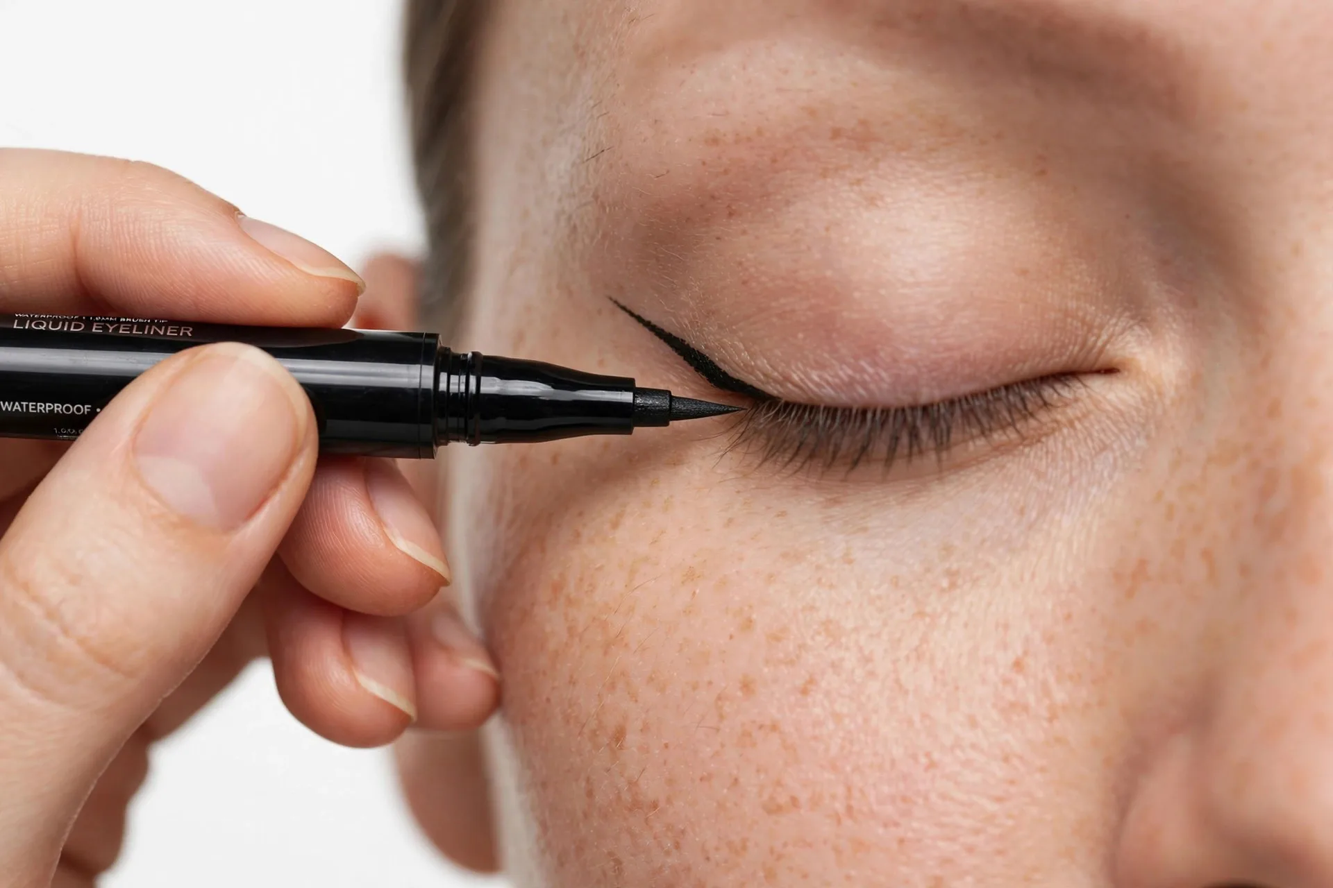 Applying black liquid eyeliner pen to create a wing on a closed hooded eye